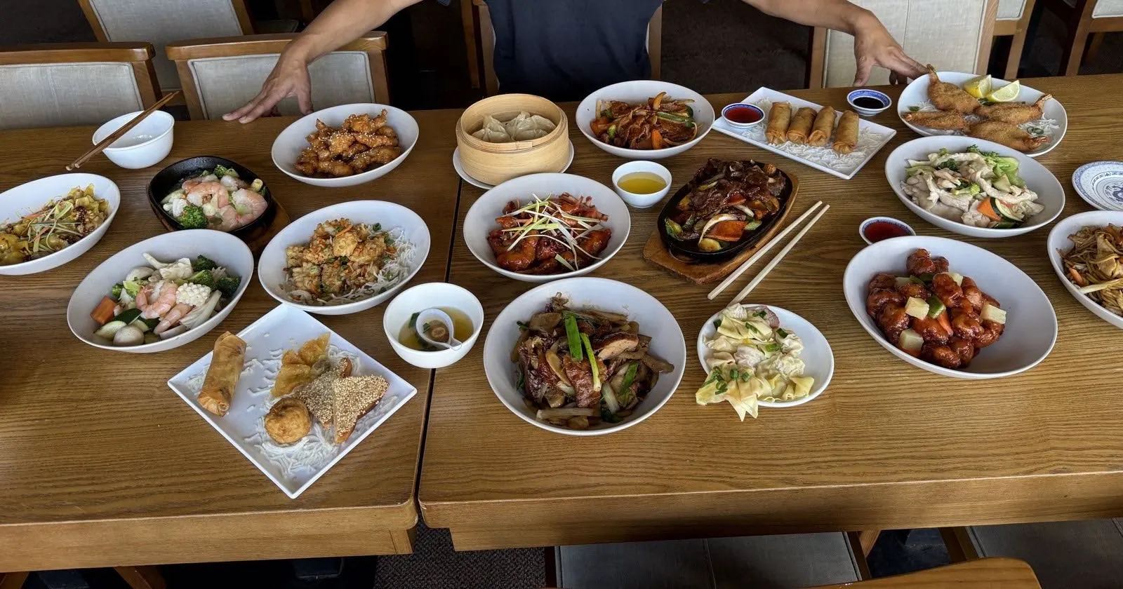 Welcoming arms over a table laden with fourteen freshly cooked Cantonese dishes